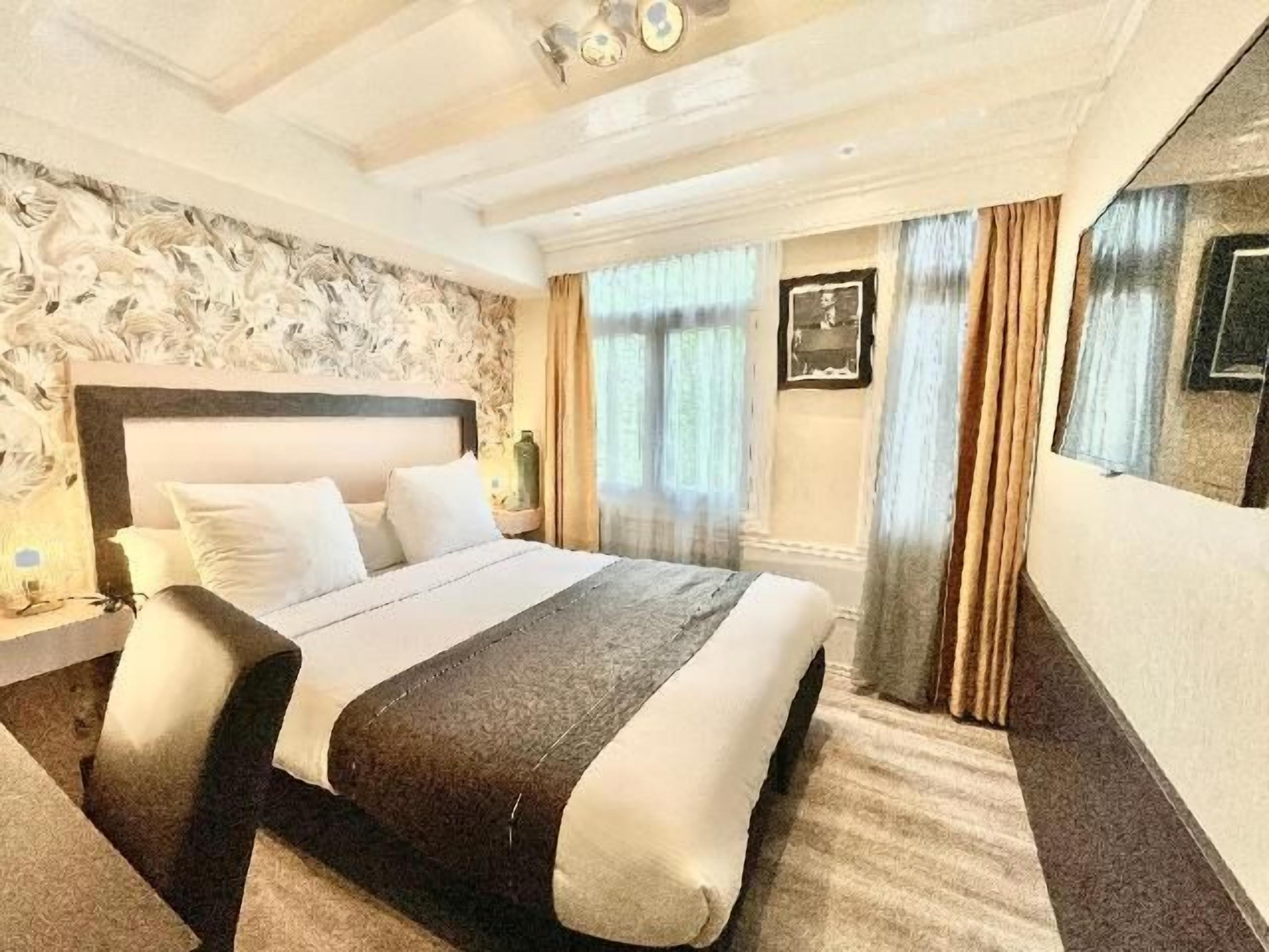 A hotel room with a large bed, a headboard, a bedside table, a mirror, and curtains.