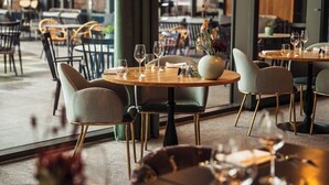 A restaurant interior with round tables, chairs, and a vase with flowers. - Hotel Venlo (Venlo)