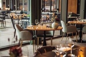 A restaurant interior with round tables, chairs, and a vase with flowers. - Hotel Venlo (Venlo)