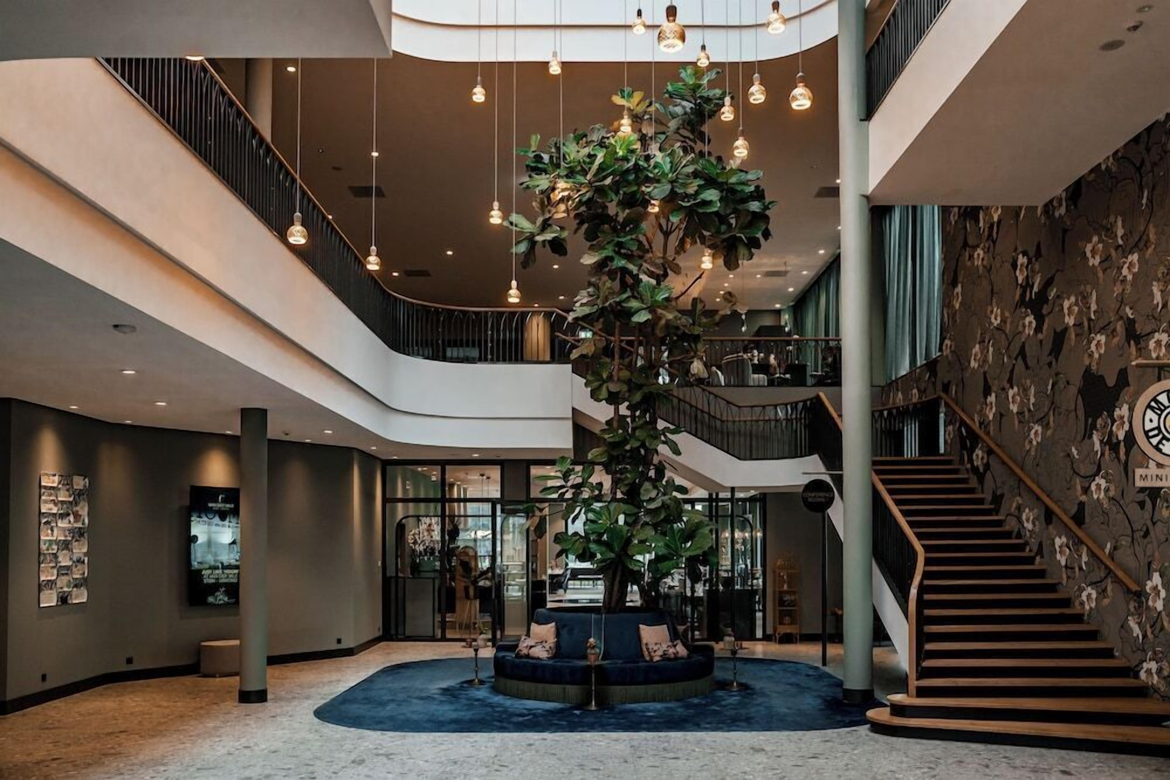 Un hall d’entrée moderne avec un espace salon central, un escalier et une grande plante.