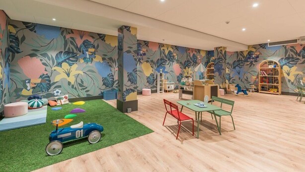 A spacious children's playroom with a green carpet, colorful play area, and a large bookshelf. - Hotel Venlo (Venlo)