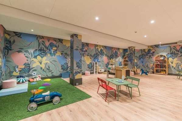 Une salle de jeux spacieuse pour enfants, avec un tapis vert, un espace de jeux coloré et une grande bibliothèque.