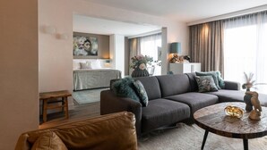A modern living room with a sofa, a coffee table, and a bench. There is a painting on the wall and a vase with flowers on a table. - Hotel Venlo (Venlo)