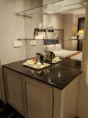 Une chambre d’hôtel dotée d’un grand miroir, d’un plan de travail noir avec une machine à café, un service à thé et un plateau contenant divers condiments.