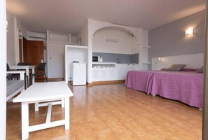 Quarto compacto com cama, pequeno espaço de cozinha, mesa de jantar e uma cadeira.