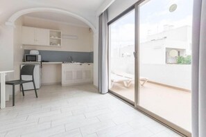 Cozinha moderna com armários brancos, micro-ondas e pia. Há uma área de jantar com mesa e cadeiras. Uma grande porta de vidro deslizante dá acesso a um pátio externo.