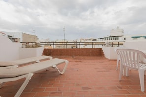 Eine Dachterrasse mit Backsteinmauer, zwei weißen Liegestühlen und Blick auf umliegende Gebäude.