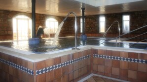 An indoor swimming pool with multiple water jets, stone walls, and tiled flooring. - Hotel Balneario De Corconte (Valle De Valdebezana)