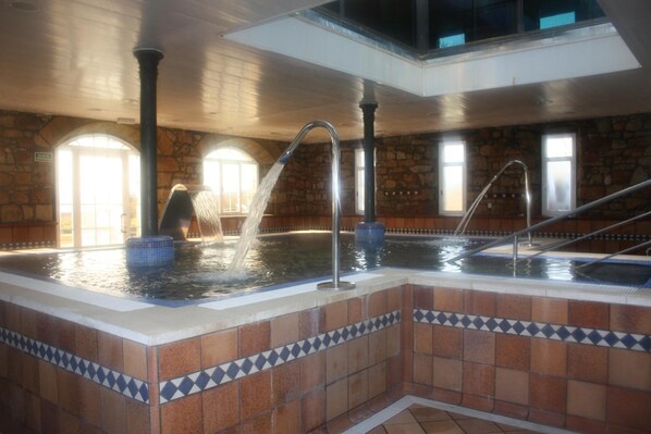An indoor swimming pool with multiple water jets, stone walls, and tiled flooring. - Hotel Balneario De Corconte (Valle De Valdebezana)