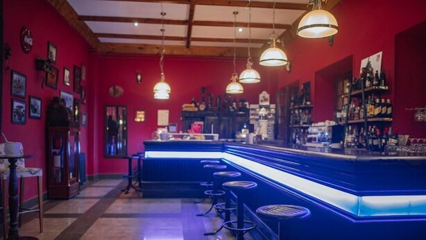 A bar area with a blue neon-lit counter, multiple stools, and hanging pendant lights. - Hotel Balneario De Corconte (Valle De Valdebezana)