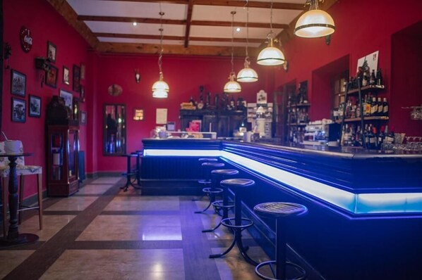 A bar area with a blue neon-lit counter, multiple stools, and hanging pendant lights. - Hotel Balneario De Corconte (Valle De Valdebezana)