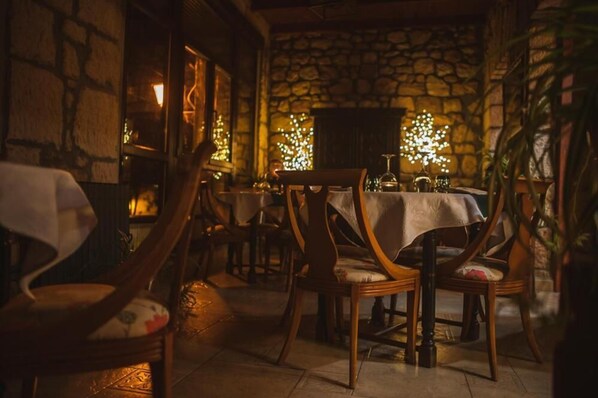 Een gezellig restaurant met stenen muren en houten meubels. Tafels zijn gedekt met witte tafelkleden en kaarsen.