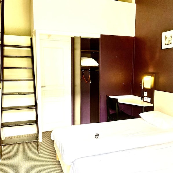A hotel room with a bed, a desk with a lamp, a chair, and a wardrobe. - Balladins Lyon Dardilly (Dardilly)