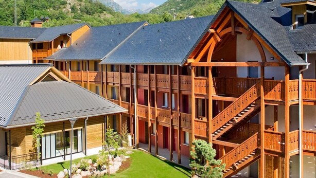 A multi-story wooden building with balconies and a staircase, surrounded by mountains and greenery. - Lagrange Confort Les Chalets D Apos Ax (Ax-les-Thermes)