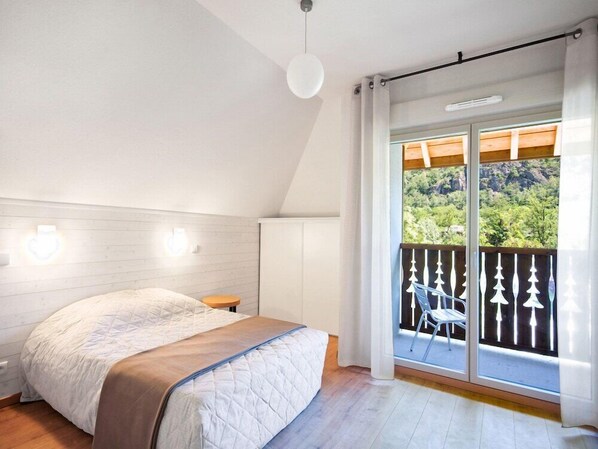 Un dormitorio con cama, una mesita y un balcón con vistas a zonas verdes.