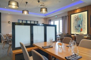 A modern conference room with a large table, chairs, and a glass partition. There are ceiling lights, a framed artwork on the wall, and a window with curtains. - Brit Hotel Restaurant Le Cottage (Arnage)