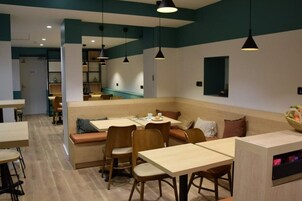 Un espace repas moderne avec des tables et des bancs en bois, un éclairage suspendu et une palette de couleurs neutres.