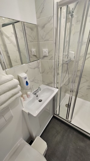 Ein Badezimmer mit einer Duschkabine, einem Waschbecken mit Seifenspender und einem Spiegel über dem Waschbecken.