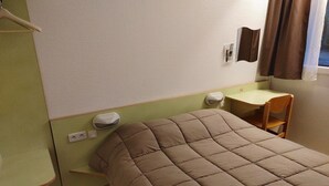 Una cama individual con cabecera acolchada en una habitación con pared verde, un escritorio pequeño y una silla.