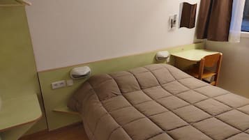 A single bed with a quilted headboard in a room with a green wall, a small desk, and a chair.