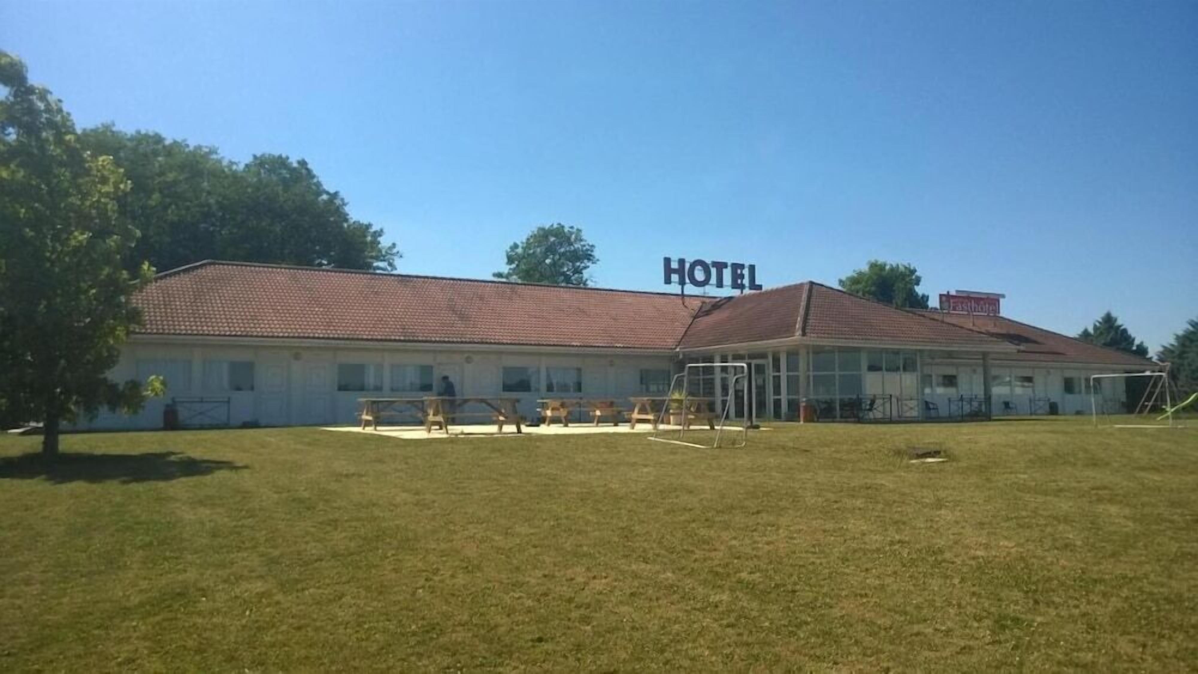 A hotel with a red-tiled roof, a covered outdoor seating area, and a grassy lawn.