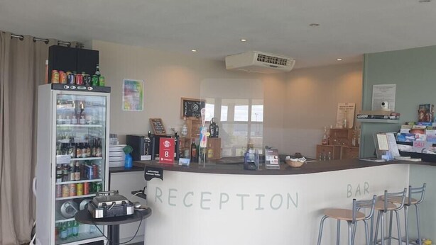 Un área de recepción con mostrador, un refrigerador lleno de bebidas y una zona de bar con taburetes.