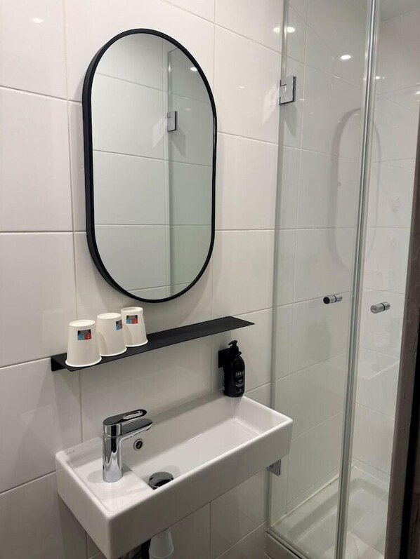 A modern bathroom with a white sink, a black-framed mirror, and a glass shower enclosure. - Hotel de L'exposition Republique (Paris)
