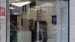 Une devanture de magasin avec une grande vitrine qui reflète la façade d’un immeuble et une voiture garée.