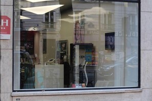 En butiksfasad med ett stort glasfönster som speglar en byggnadsfasad och en parkerad bil.