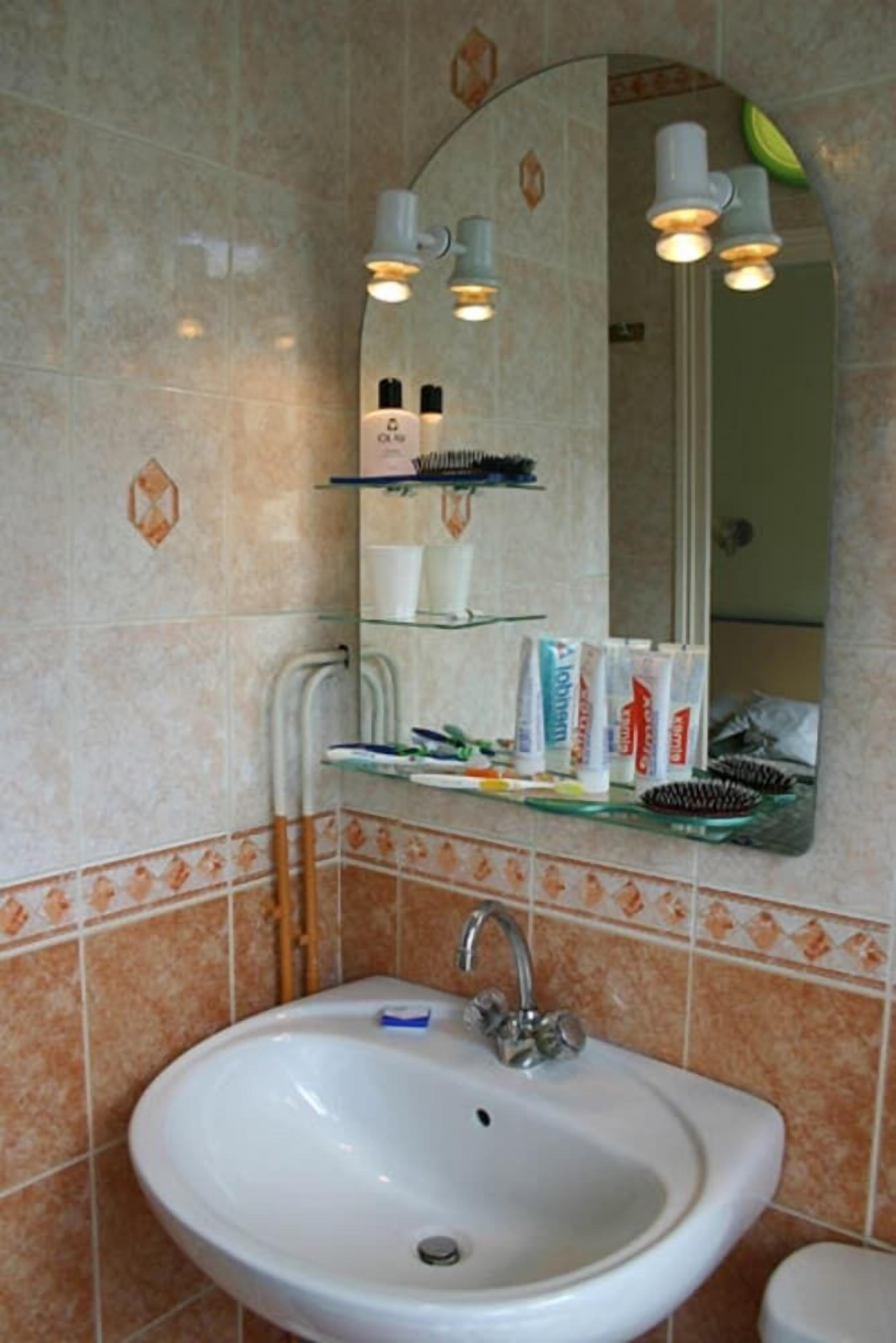 Un baño con un lavabo blanco, un espejo y repisas con artículos de aseo.