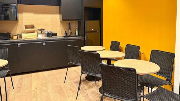 A modern kitchen with dark cabinetry and a yellow accent wall, featuring a central island with a sink and a small refrigerator.