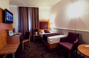 Habitación de hotel con cama, escritorio con silla, televisor y una mesita.