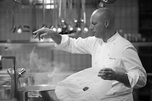 A chef in a professional kitchen with stainless steel equipment and hanging pots. - Beau Rivage Neu (Neuchatel)