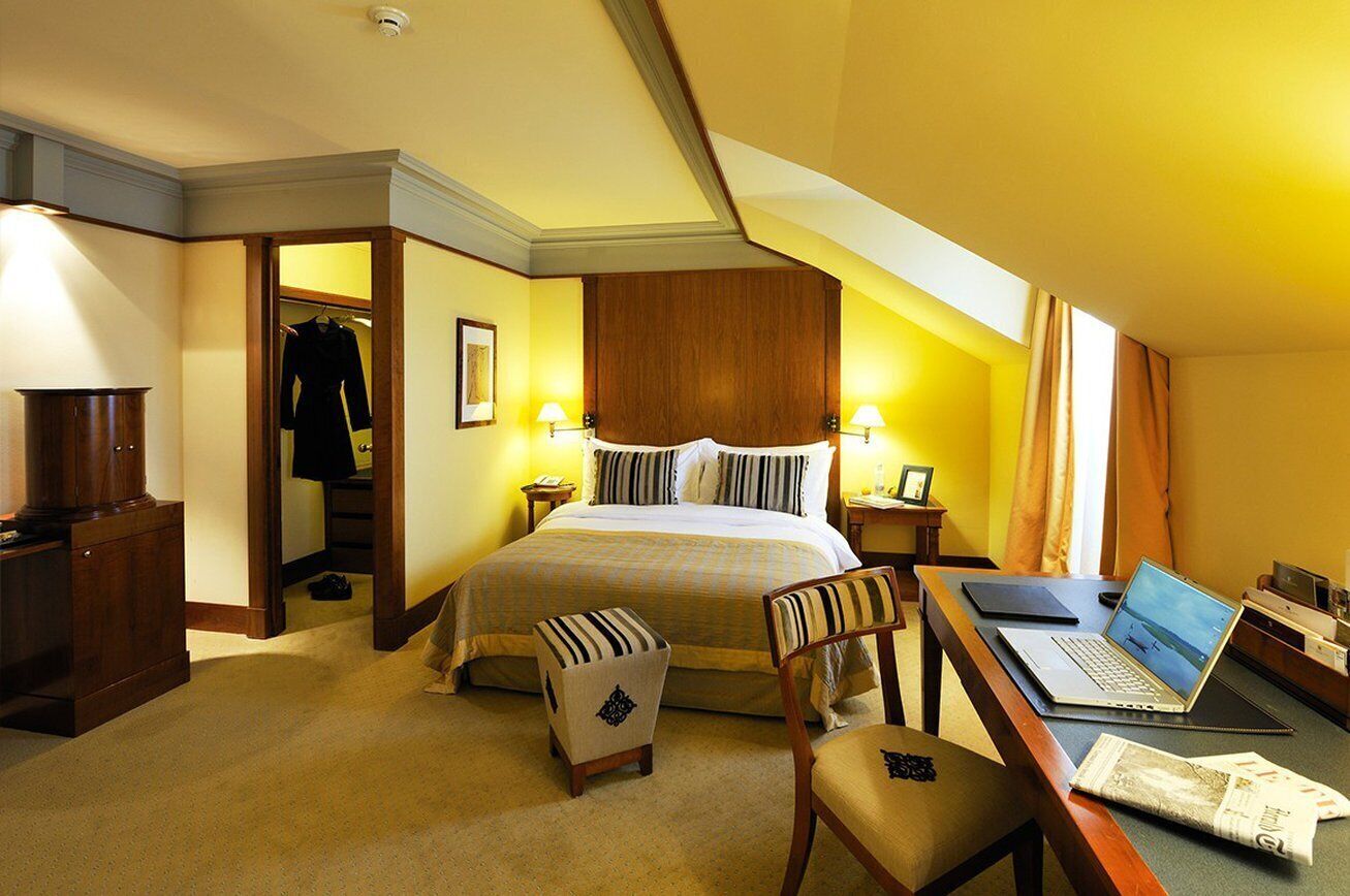 A hotel room with a bed, a desk with a laptop, a chair, a coat rack, and a wardrobe.