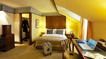 A hotel room with a bed, a desk with a laptop, a chair, a coat rack, and a wardrobe.