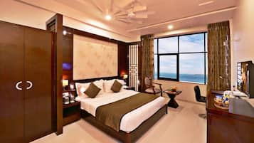 A hotel room with a large bed, a desk with a TV, a chair, a window with a view, and a wardrobe.