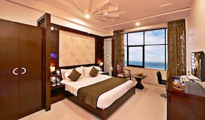A hotel room with a large bed, a desk with a TV, a chair, a window with a view, and a wardrobe. - Lords Eco Inn Porbandar (Porbandar)