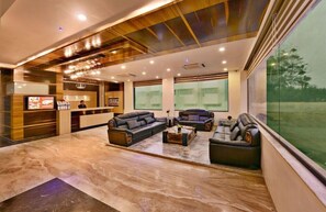 A modern lobby with leather sofas, a reception desk, and large windows offering a view of the outdoors. - Lords Eco Inn Porbandar (Porbandar)