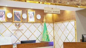 A reception desk with a sign reading "Reception" and "Welcome". There are framed pictures above the desk, a flag, and a logo for Landmark Hotel Suites. - Landmark Hotel Suites (Tabuk)