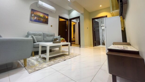 A modern living room with a grey sofa, a white coffee table, and a painting on the wall. - Landmark Hotel Suites (Tabuk)