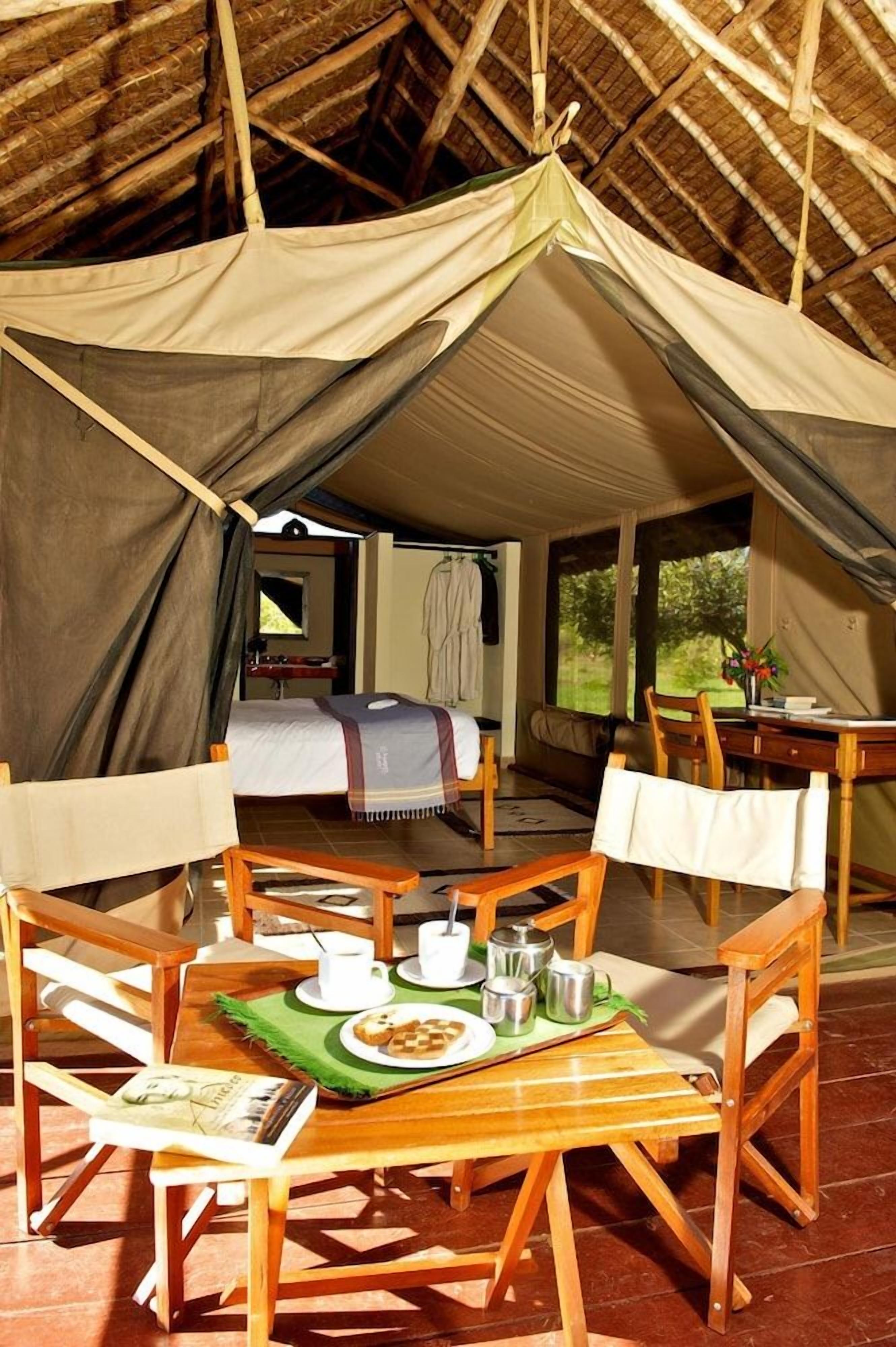 A tented accommodation with a dining table, chairs, and a bed.