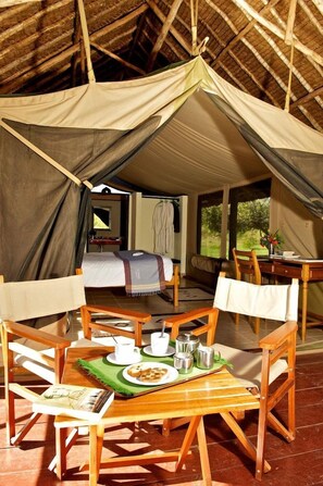 Acomodação em tenda com mesa de jantar, cadeiras e cama.