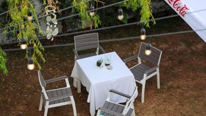 Un área de estar al aire libre con una mesa y cuatro sillas, rodeada de follaje y luces colgantes.