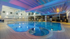 Piscina interior com chão ladrilhado, prancha de salto e teto com tubulações aparentes.