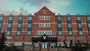 Um edifício de vários andares com uma entrada imponente, uma placa com o logotipo 'V' e uma placa da Starbucks no andar térreo.