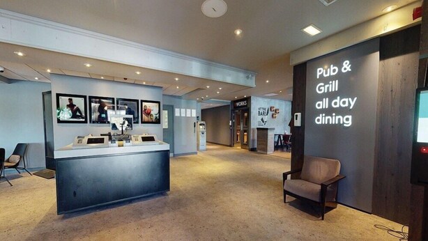 Uma área de recepção com balcão, assentos e um painel com a inscrição 'Pub & Grill - Refeições o dia todo'.