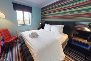 Una camera d'albergo con un letto, una sedia rossa, una scrivania e una finestra.