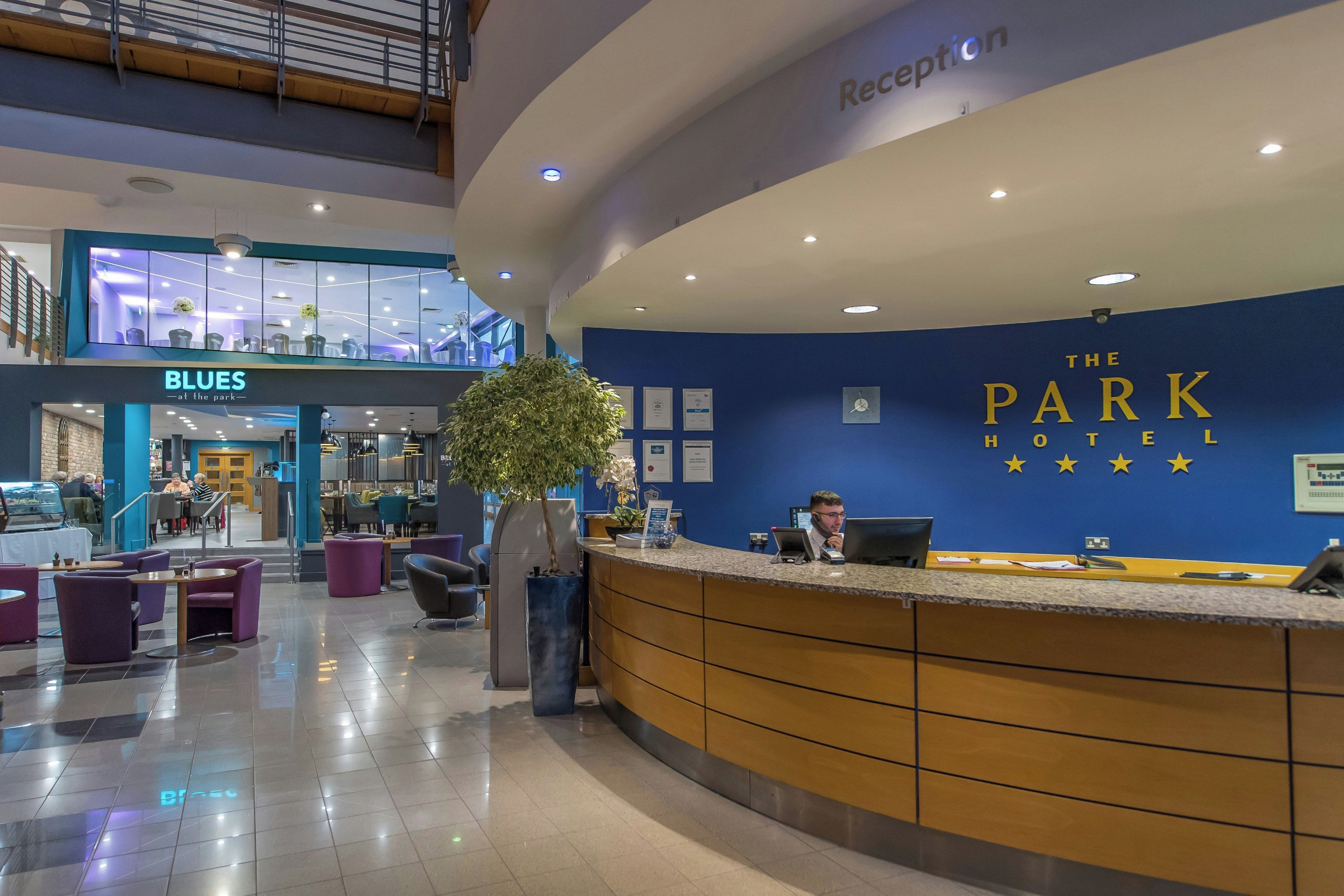 A hotel reception area with a blue wall, a reception desk, and a seating area with purple chairs.