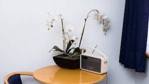 Een kleine ronde tafel met een radio, twee stoelen en een orchidee in een pot.