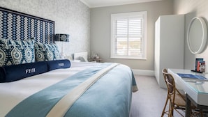 A hotel room with a large bed, a desk with a chair, a window with blinds, and a wall-mounted mirror. - The Fowey (Fowey)